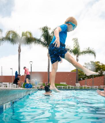 A child jumps into a pool as a counselor stands with outstretched hands