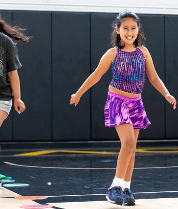 A child smiles as she skips in a gym