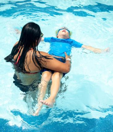 An adult holds child floating on back in water