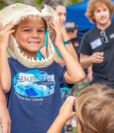 young child holding a large shark jaw up to their face and smiling