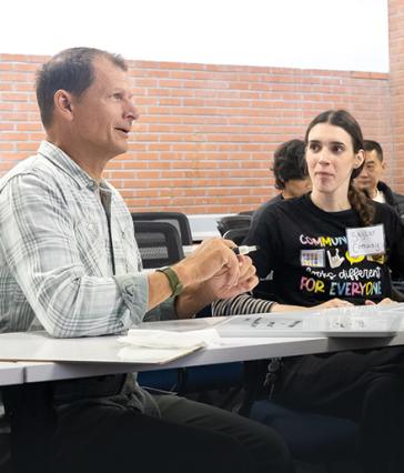 Two people talk at a desk with whiteboards during class