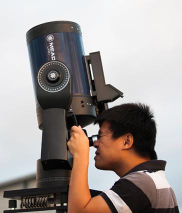 A student peers through a large telescope pointing upwards