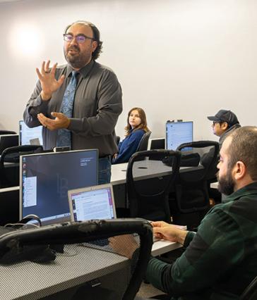 A person wearing glasses and a tie speaks in front a class