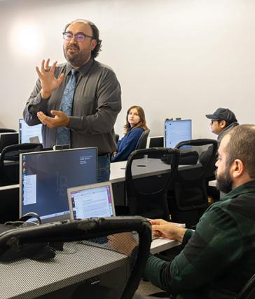 A person wearing glasses and a tie speaks in front a class