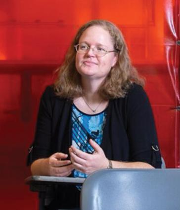 A person sits at a school desk with a red background