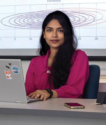 A student with long hair at a computer with a slide projected behind her