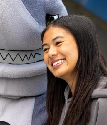 A person with long hair poses with a mascot