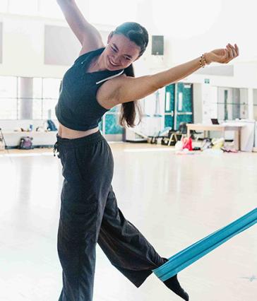 A person balances on one foot with arms extended and blue fabric attached to foot