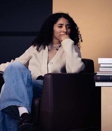 A person sits in a chair with a stack of books nearby