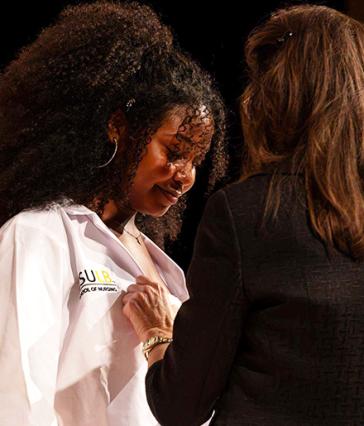 A student receiving a faculty member's help donning a lab coat