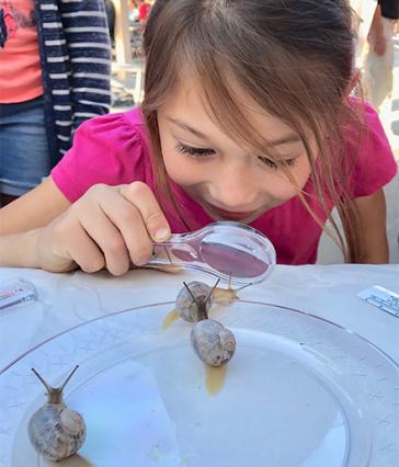 young child using a magnifying glass to examine a snail