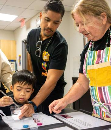 A child stirs a cup as an adult and instructor help.