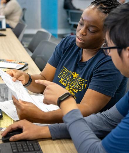 A woman in a "Rams Track & Field" shirt reviews a tax document with an accounting student at the VITA lab.