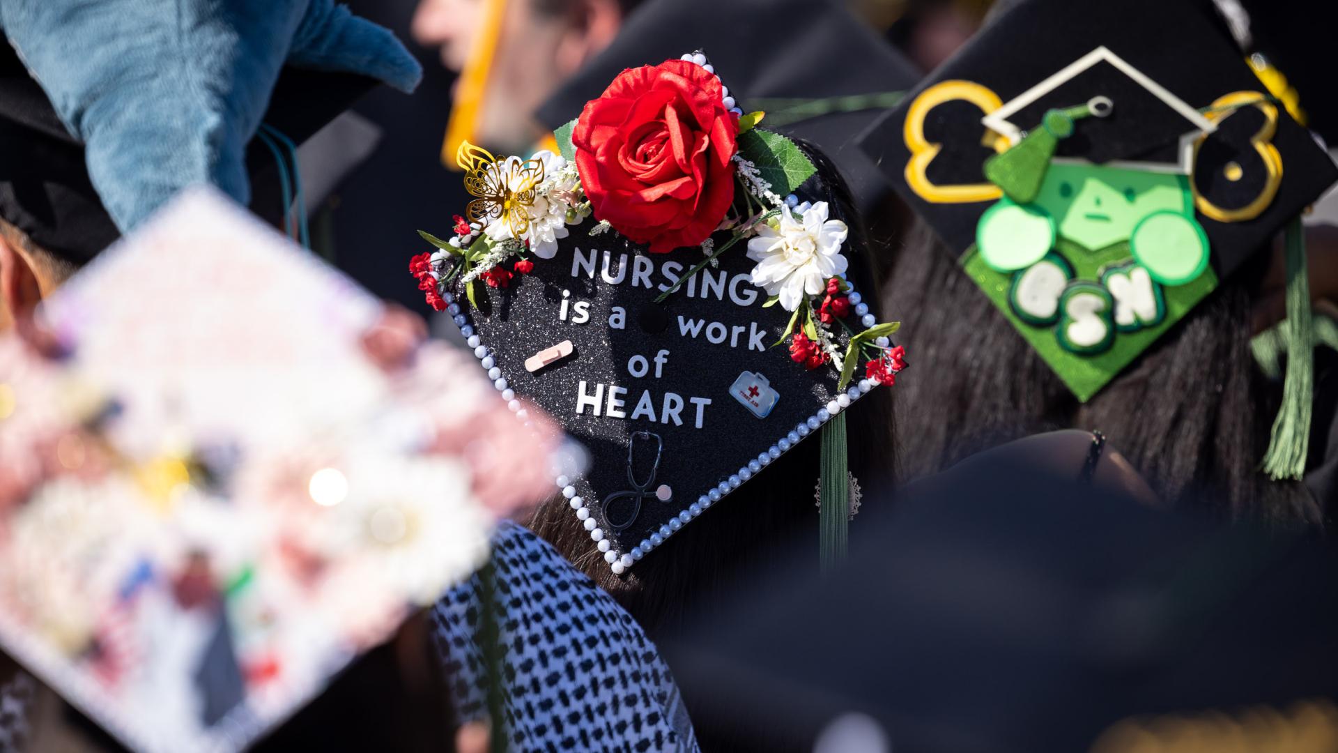 Graduation cap reading "Nursing is a work of heart" decorated with red rose