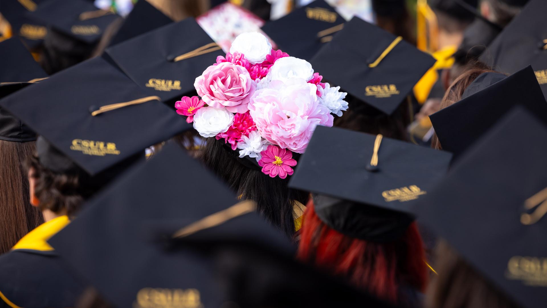 Graduation cap decorated with pink and white flowers among CSULB caps