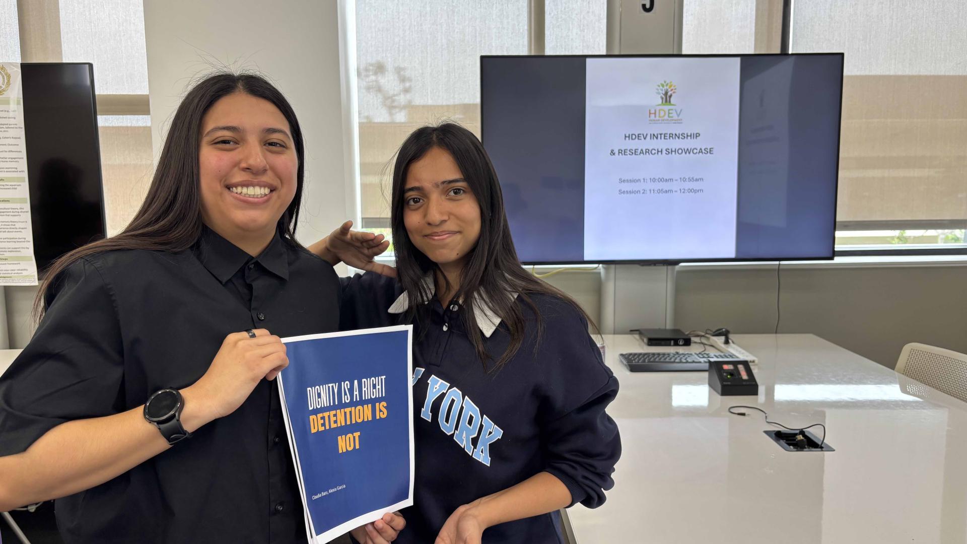 2 Students smiling while holding up paper poster of their research