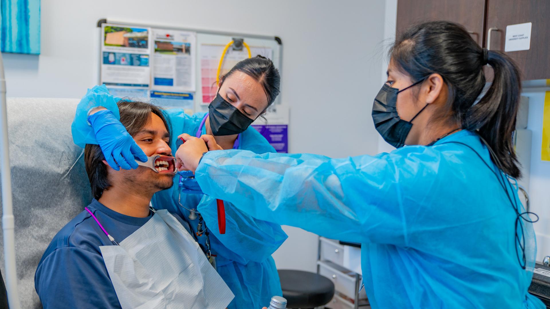 A student getting his teeth checked by two dentists.