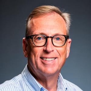 Headshot of Joseph Aubele. Wearing glasses with striped collared shirt.