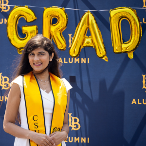CSULB grad in front of gold GRAD balloons CSULB grad in front of gold GRAD balloons