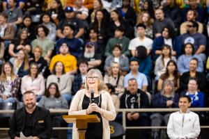 President Jane Close Conoley with a microphone speaking with a large crowd seated behind her
