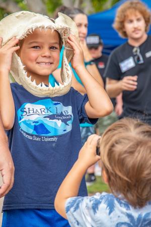 Child at Day at The Beach Child pokes head through a pair of shark jaws while wearing Shark Lab t-shirt