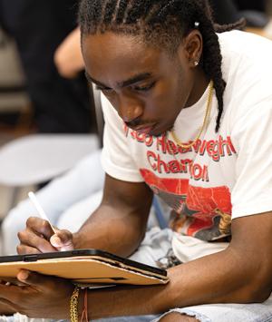 A student in a T-shirt writes on an iPad