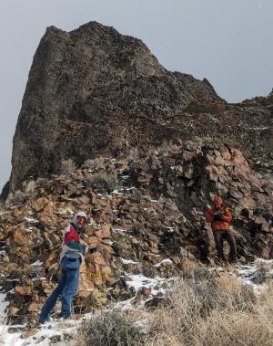 two people standing on a rocky mountainside with patches of snow