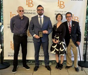 Faculty and student at an awards ceremony. Student holding an award by a CSULB backdrop.