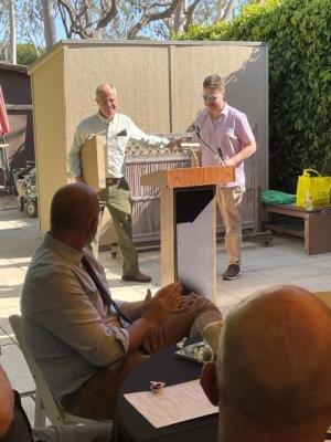 Two people are smiling and standing at a podium. They are fa