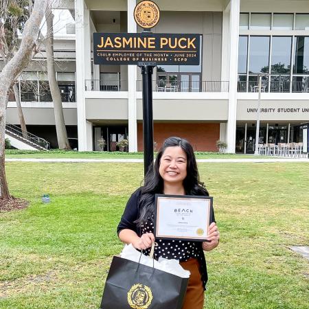 Employee of the Month Jasmine Puck Jasmine Puck stands beneath the Employee of the Month sign on campus