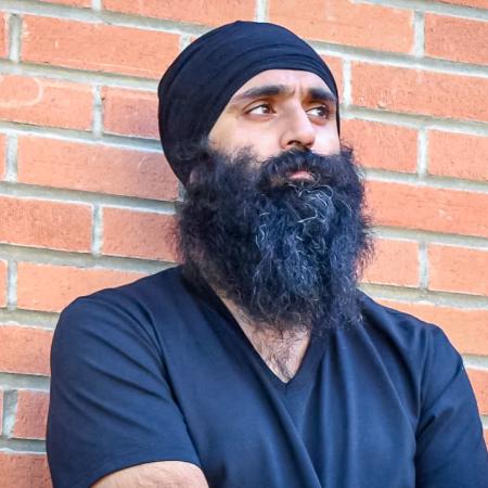 Rajbir Singh Judge A person with a long beard and wearing a black turban leans against a brick wall with arms crossed.