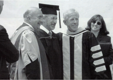 Steven Spielberg receives his diploma Three people in academic robes smile at a graduation ceremony.