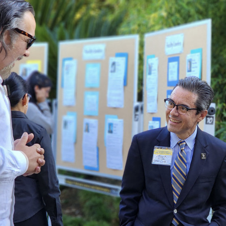 College of Engineering dean Mark Suazo, left, in front of the 'Wall of Wow' Two men speak in font of bulletin boards containing photographs and text.