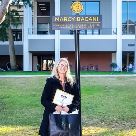 January 2025 Employee of the Month Marci Bacani stands besides a campus sign bearing her name. January 2025 Employee of the Month Marci Bacani stands besides a campus sign bearing her name.