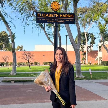 A woman holds flowers and stand in front of a sign that says "Elizabeth Harris"