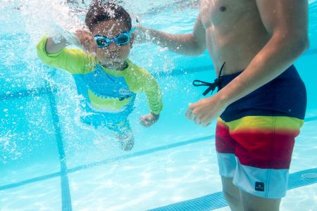 Child swims underwater near an adult's hand