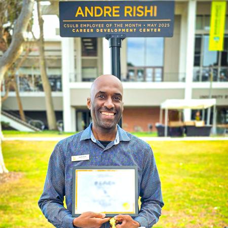 Andre Rishi Employee of the Month Andre Rishi holds a certificate and smiles under a sign with his name.