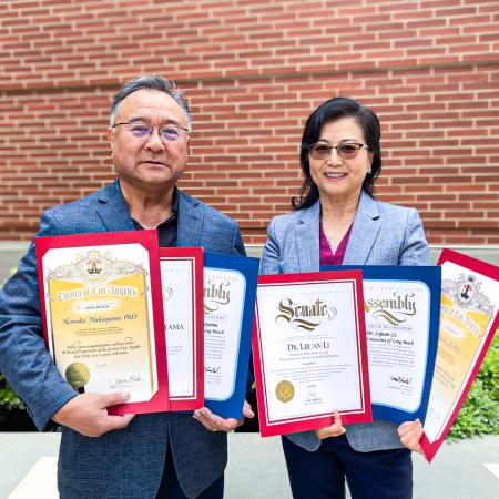 Kensaku Nakayama, left, and Lijuan Li Two people hold framed certificates while standing in front of a brick wall.