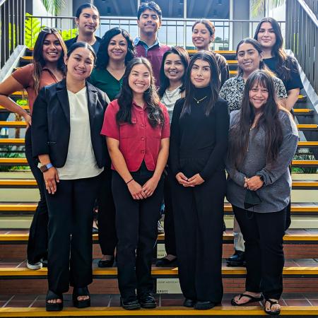 ÁNDALE students on stairs Group of thirteen people stand on indoor stairs smiling at the camera.