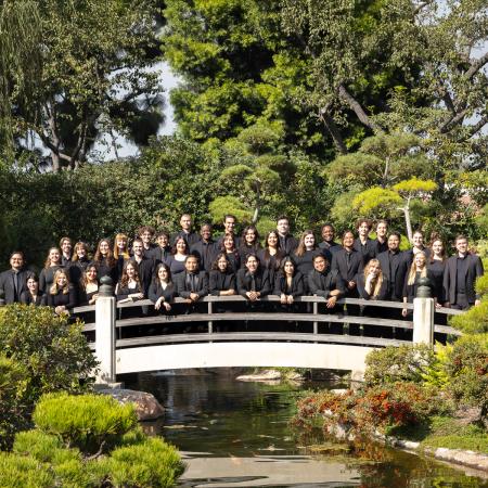 CSULB Chamber Choir in Japanese Garden Large group in black clothing stands on a bridge over water in a garden.