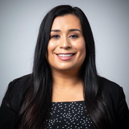 Portrait of a person smiling in front of a gray background.