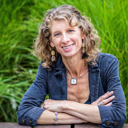Professor Gwen Schaffer A person smiles outdoors with arms crossed at a table