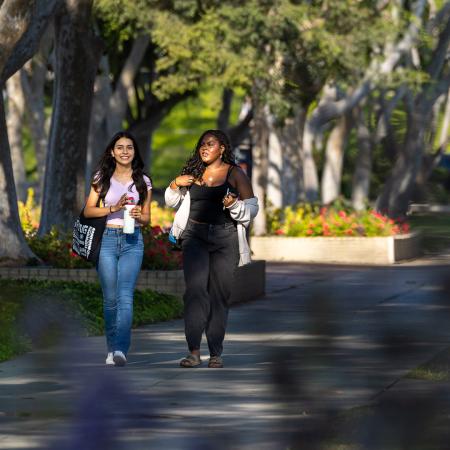 Campus scene Two people walk on campus among trees