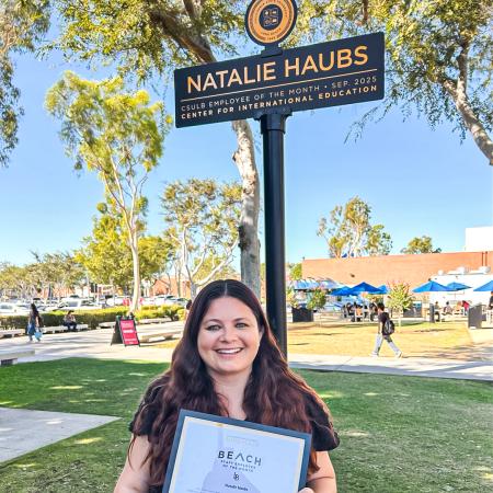 Employee of the Month Natalie Haubs Employee of the Month Natalie Haubs stands on the CSULB campus holding an award beneath a sign with her name.