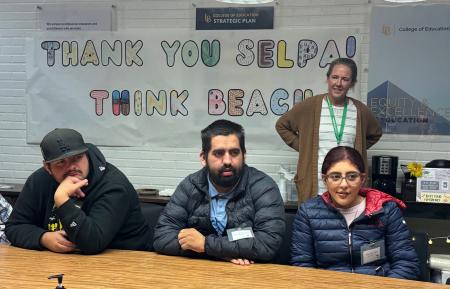 Students sit at a conference table and listen to a speaker