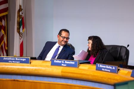 Two city officials speak during a council meeting
