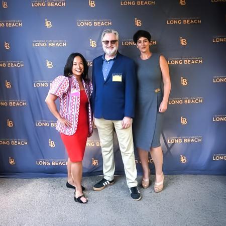 Three people stand smiling in front of a CSULB backdrop.