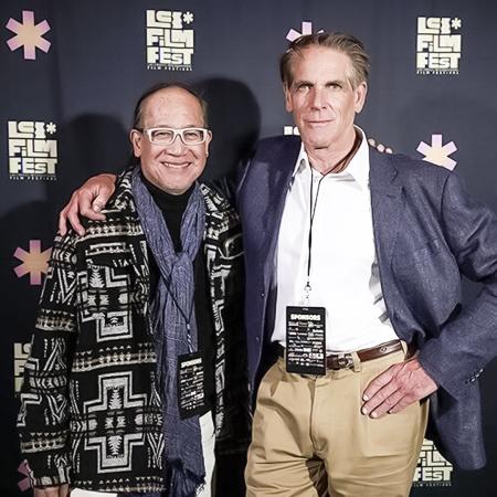 Two people stand together smiling in front of an LB film festival backdrop.