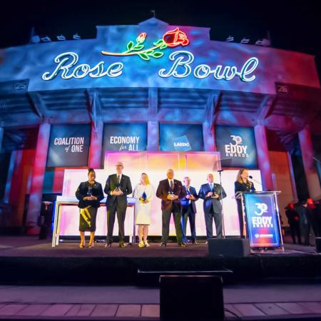 A group of people stand onstage holding awards beneath a large Rose Bowl sign.