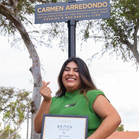 Employee of the Month Carmen Arredondo stands under a sign with that name while holding an award.